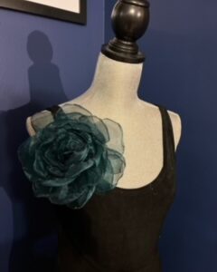 Black dress with a large teal floral shoulder embellishment on a mannequin.