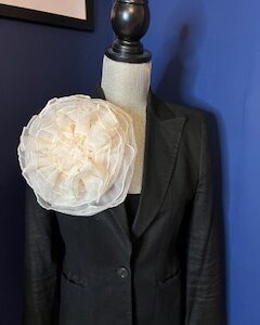 Black blazer with a large white floral accessory on the shoulder.