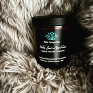 A black candle jar with a lotus logo on a soft, furry surface.