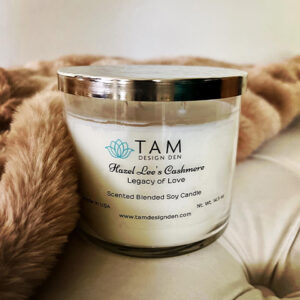 A scented candle in a glass jar with a silver lid, placed on a soft fur.