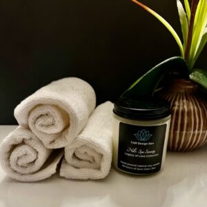 Rolled white towels with a spa candle and plant on a glossy surface.