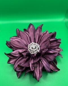 A purple fabric flower with a decorative white center on a green background.