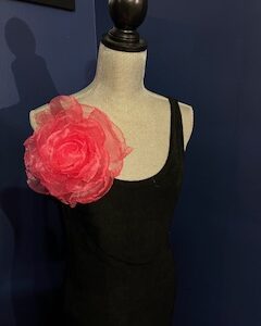 Black dress with a large pink floral accessory on the shoulder.
