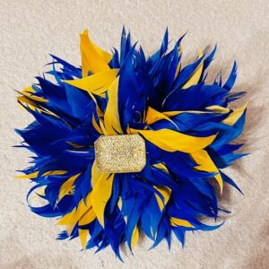 A vibrant blue and yellow feathered decorative piece with a central jeweled embellishment.